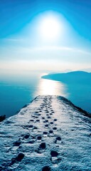 Snowy clifftop path leading to a bright sunlit ocean
