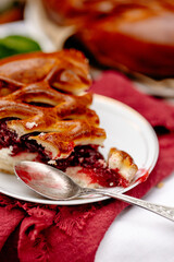 Traditional cherry pie with glossy braided crust and juicy red filling, set with cup of tea on rustic fabric. Perfect for editorial or packaging use.