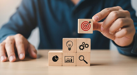 Person placing target block on stacked wooden cubes with business icons lightbulb gears