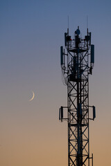 Cell tower and crescent moon at sunset vertical