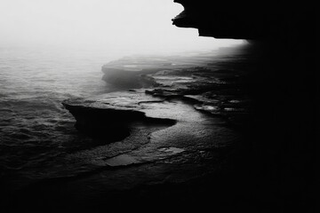 Misty coastal cave opening, dark rocks, rough waves