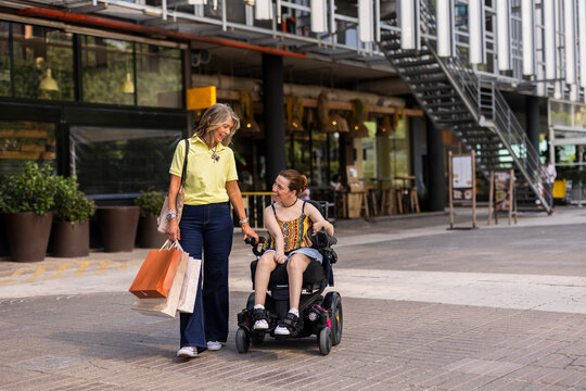 Woman pushing friend in electric wheelchair after shopping spree