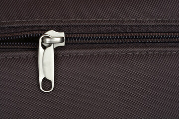 A close-up shot of a silver zipper pull on dark brown textile, revealing its metallic texture and the fine stitching around the opening © nahhan