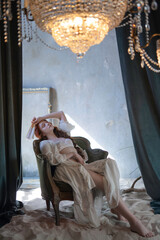 A languid girl with a fan in lingerie and a negligee on a vintage chair