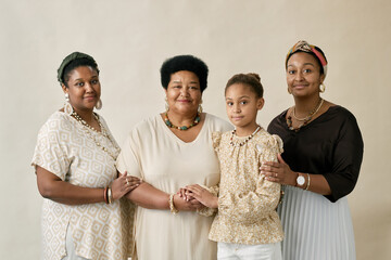 Portrait of three African American women and girl in casual outfits posing together in studio against neutral background