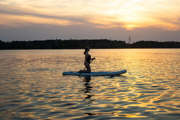 Woman poses on a sup board with paddle. Sunset in the background. Copy space. Concept of sup...