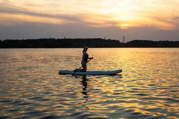A young woman poses on a sup board with paddle. Sunset in the background. Copy space. Concept of...