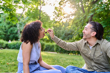 Happy couple sharing cherries during romantic picnic in park