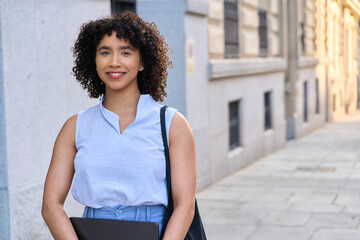 Smiling businesswoman holding laptop walking on city street