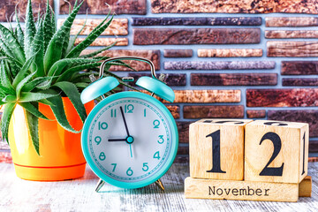Wooden calendar with the date November 12.Monthly calendar for planning and management concept with alarm clock on wooden background