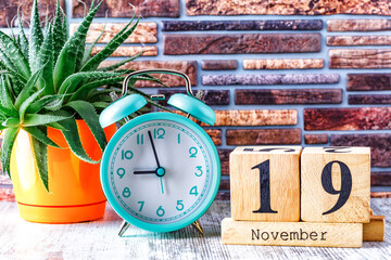 Wooden calendar with the date November 19.Monthly calendar for planning and management concept with alarm clock on wooden background