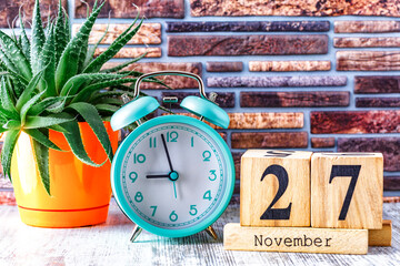 Wooden calendar with the date November 27.Monthly calendar for planning and management concept with alarm clock on wooden background