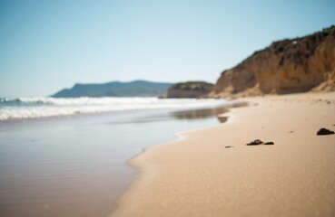 A peaceful sandy beach with gentle waves and distant cliffs under a clear sky