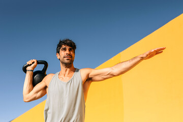 Hispanic man exercising with kettlebell in outdoor urban setting during bright daylight