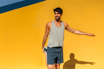 Hispanic man stretching during outdoor workout against vibrant yellow wall