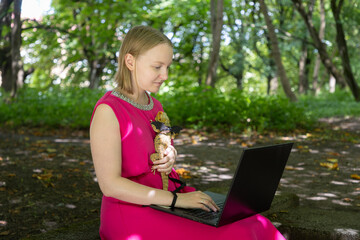 Young woman working on her laptop in a summer park gently cradles her harnessed agama lizard in a tender embrace