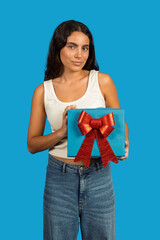 Young woman holding a gift box with red bow on blue background