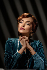 Beautiful charming woman with evening make-up and jewelry posing on dark background. Girl in retro style dress and necklace posing with feather fan and veil headdress in studio setting