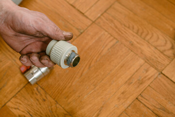 Closeup photo of male plumber holding polypropylene compound for pipes. Plumbing maintenance in progress, worker securing pipe joint with tow and wrench