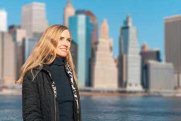 Pretty happy woman on downtown skyline background with skyscrapers. Cityscape and river scene with woman in focus, tall buildings and sunny weather visible.