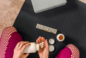 Female hands sorting her daily vitamins for healthy lifestyle. Fitness routine at home, female organizing pills and capsules on black exercise mat