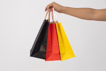 A hand holds three shopping bags in the colors black, red, and yellow, arranged from left to