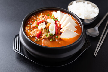 Korean food (Kimchi Jjigae), Kimchi soup with tofu, pork, scallion and chili in Korean stone bowl eating with cooked rice on black background