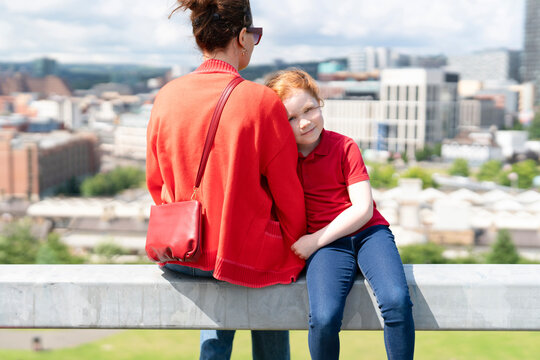 Mother and child enjoying a sunny day at a city viewpoint, overlooking urban landscape with modern buildings in the background