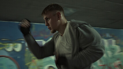 A determined Caucasian male athlete in a gritty gym practices boxing with intense focus. His dynamic stance and blurred motion convey relentless training, surrounded by vibrant graffiti.