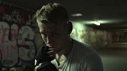 Close-up of a focused Caucasian male athlete in a white t-shirt and black gloves, standing in a...