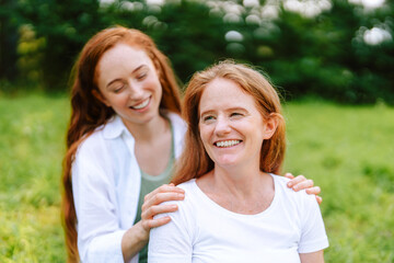 Obraz premium Two women mother and daughter enjoying a sunny day outside, sharing smiles and laughter in a green park setting during the afternoon