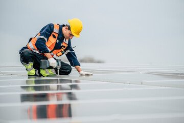 Worker installs solar panels on rooftop during overcast day while ensuring safety and precision in...