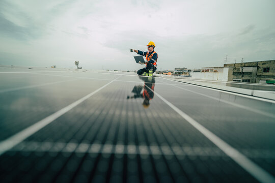 Solar technician inspects photovoltaic panels on rooftop in urban setting during cloudy day