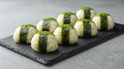 Several onigiri rice balls with seaweed and matcha powder are on a slate plate