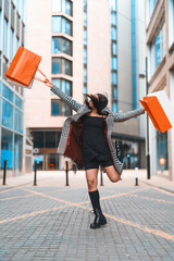 Woman joyfully shopping in urban center, showcasing her purchases while wearing stylish outfit and...