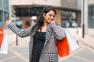 Woman enjoys shopping in urban environment, showcasing vibrant bags and bright smile on a sunny day