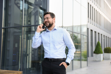Happy businessman talking on phone near office building