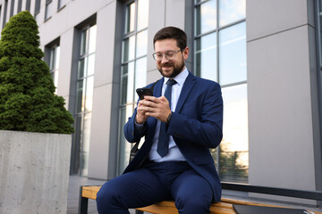 Successful businessman with smartphone near office building