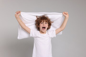 Cute little boy in pajamas with pillow on grey background
