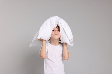 Cute little boy in pajamas with pillow on grey background
