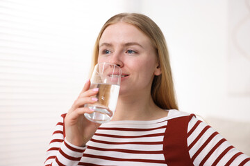 Young woman drinking water from glass at home