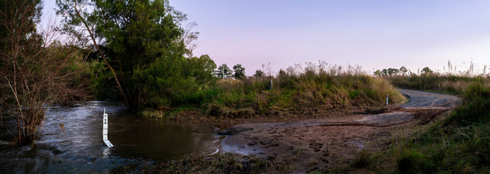Low level crossing road during flood with soil dumped and floodwaters flowing past height marker