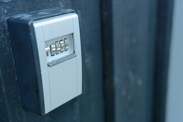 Light grey key safe wall safe with combination lock is attached to a dark wooden wall with open lid