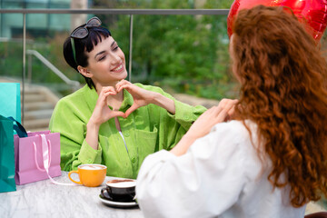 Friends celebrate friendship with coffee and heart-shaped gesture at outdoor cafe on a sunny day