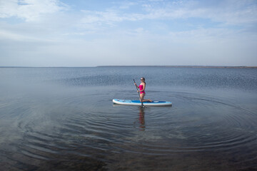 A young woman on a sup board with paddle. Sunset in the background. Copy space. Concept of sup...