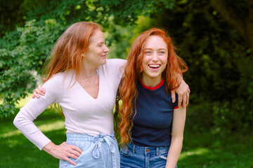 Two red-haired women mother, daughter enjoying a joyful moment together in a lush green park on a...