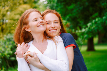 Two women mother and daughter share a joyful moment in a lush park during a sunny day, embracing...