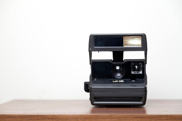 An instant camera instantly develops photos on a wooden table. Vintage camera concept. Photography concept. 
Space for text.