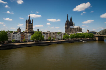 Fototapeta premium Picturesque Cityscape by the River: A stunning wide shot of a historic city, featuring grand architectural buildings, and a serene river under a bright blue sky.