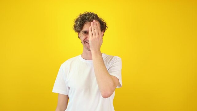 Happy man covers one eye with his hand during an eye exam on a bright yellow background ideal for optometry clinic, healthcare marketing, wellness campaigns, and World Sight Day promotions.